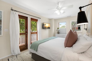 Relax in this serene bedroom with a large bed, ceiling fan, and floor lamp, offering a peaceful view of the surrounding greenery.