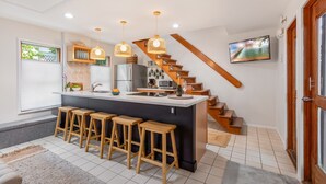 Eine moderne Küche mit einer zentralen Kochinsel, Holzbarhocker, einer Treppe und einem an der Wand befestigten Fernseher.
