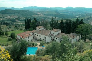 Eine Villa mit mehreren Gebäuden, einem Schwimmbad und Blick auf sanfte Hügel.