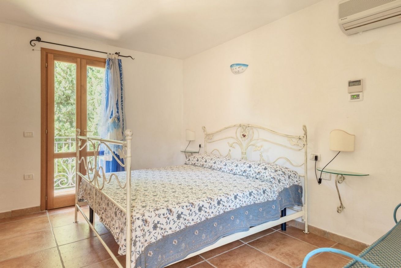 Ein Schlafzimmer mit Bett, Fenster mit Vorhang, Wand-Klimaanlage und Nachttisch mit Lampe.