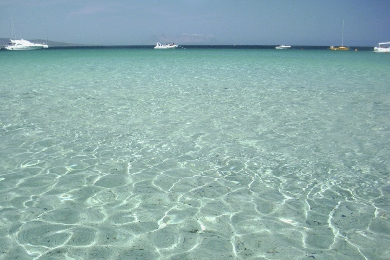 A clear turquoise sea with boats in the distance.