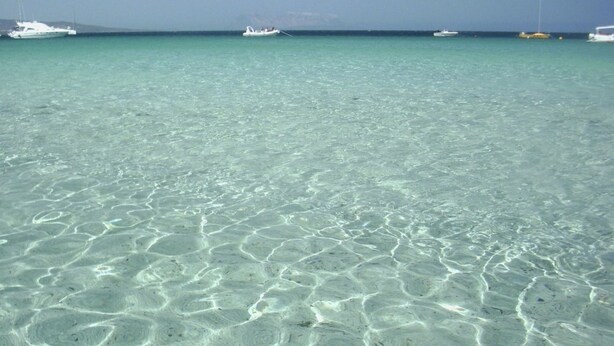 Un mar turquesa transparente con barcos a lo lejos.