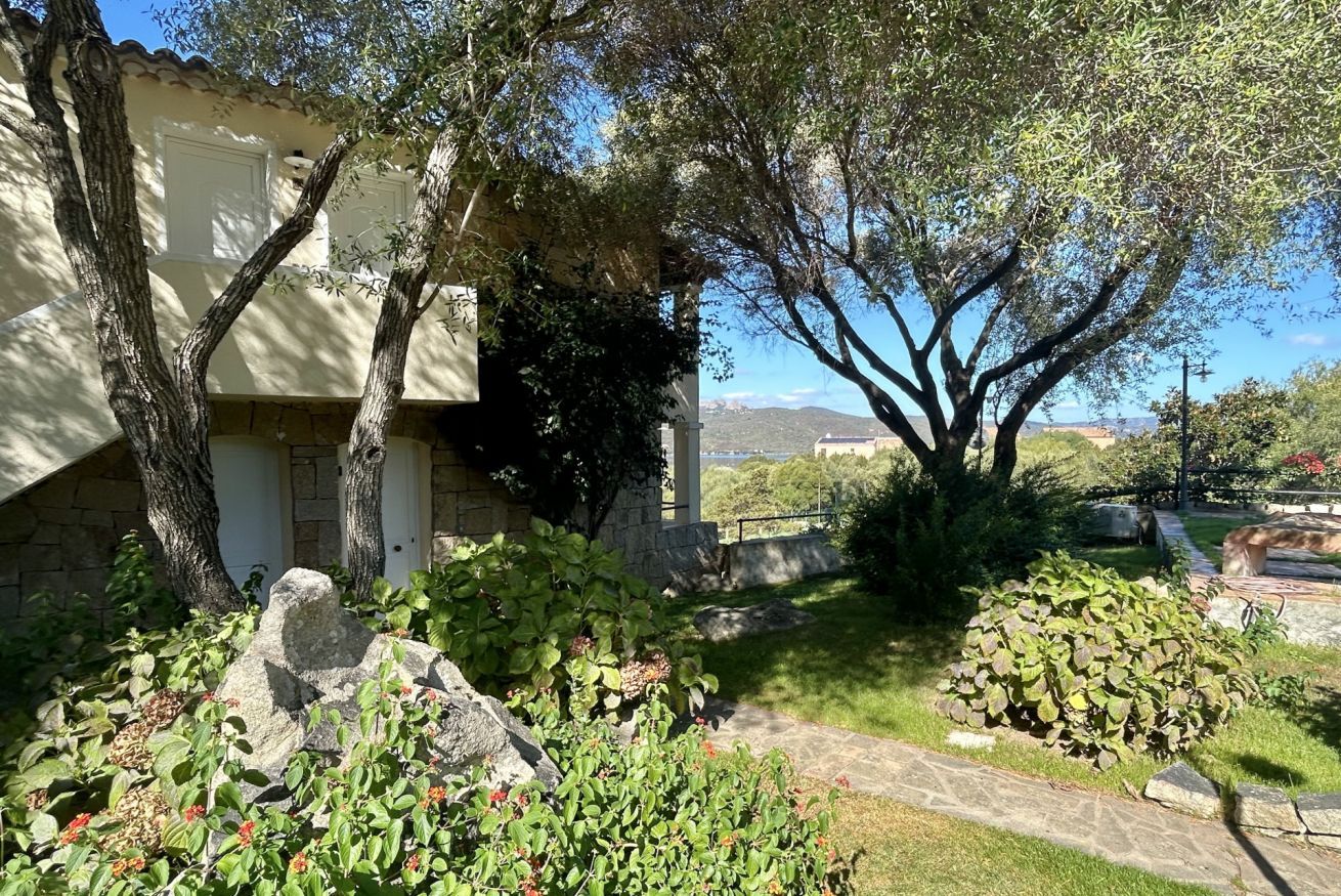 A stone building with a garden, including a large tree, a rock, and a small bush.