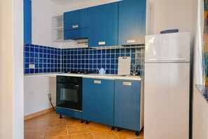 A compact kitchen with blue cabinets, a white refrigerator, and a tiled backsplash.
