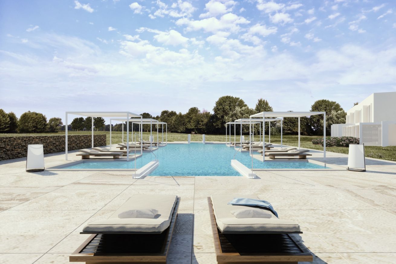Un área de piscina con sillones de descanso y sombrillas, rodeada de árboles y un cielo despejado.