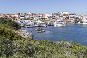 A marina with boats docked, a rocky shoreline, and buildings in the background.