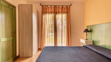 A bedroom with a bed, a nightstand with a lamp, a wooden wardrobe, and a door.