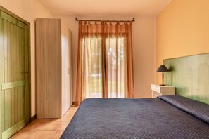 Un dormitori amb un llit, una tauleta de nit amb una làmpada, un armari de fusta i una porta.