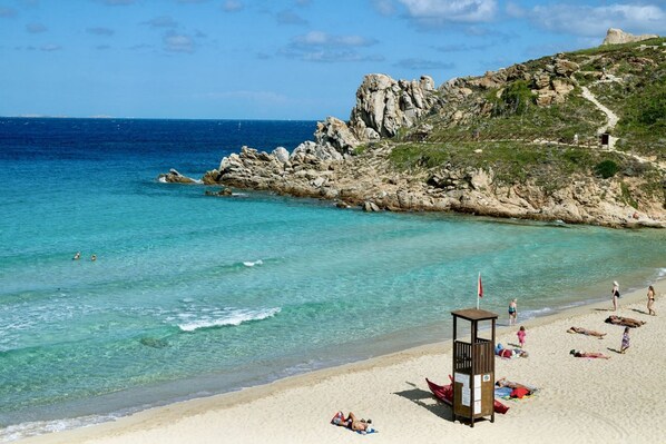Una playa con agua turquesa cristalina, acantilados rocosos y una torre de salvavidas.