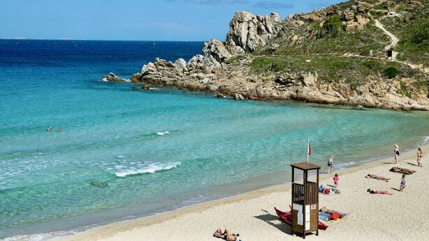 Une plage à l’eau turquoise et limpide, bordée de falaises rocheuses, avec une tour de surveillance pour les sauveteurs.