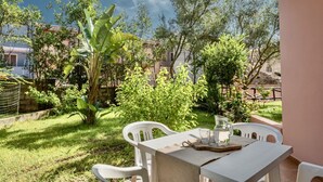 Une terrasse extérieure avec une table et des chaises, entourée de verdure et d’arbres.