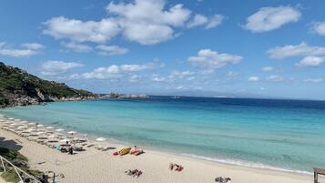 Une plage avec une eau turquoise et limpide, un rivage sablonneux et un promontoire rocheux en arrière-plan.