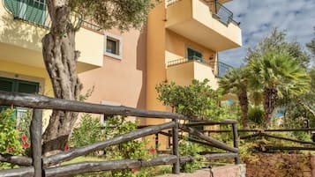 A multi-story building with balconies, a stone wall, and a wooden fence.
