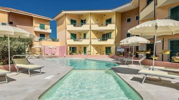 A pool area with lounge chairs and umbrellas, surrounded by multi-story buildings with balconies.