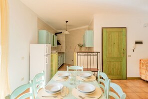 A dining area with a table set for four, light-colored chairs, and a green door in the background.