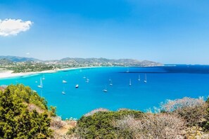 A coastal landscape with clear blue waters, boats, and a distant shoreline.