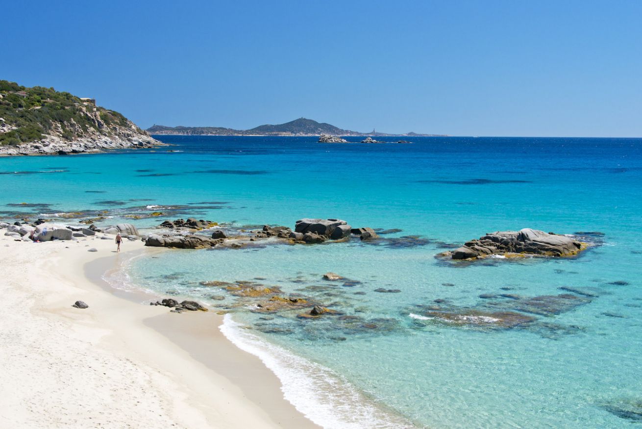 Ein Strand mit klarem türkisblauem Wasser, Felsen und einem sandigen Ufer.
