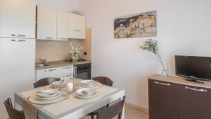 A compact kitchen with modern appliances, a dining table set for two, and a flat-screen TV on a cabinet. - Two-room apartment with 4 beds, about 45 m2, living room with kitchenette and double sofa bed, bedroom with double bed (separable beds), bathroom with toilet, bidet and shower. Possibility 1 infant in cot. <br>The charming apartments can be arranged on t (Villasimius)