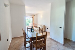 Ein Essbereich mit Holztisch und Stühlen, einer Couch und Blick ins Freie durch eine Glastür.