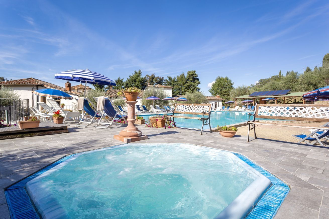 Area piscina con lettini e ombrelloni, circondata da piante in vaso e una recinzione in legno.