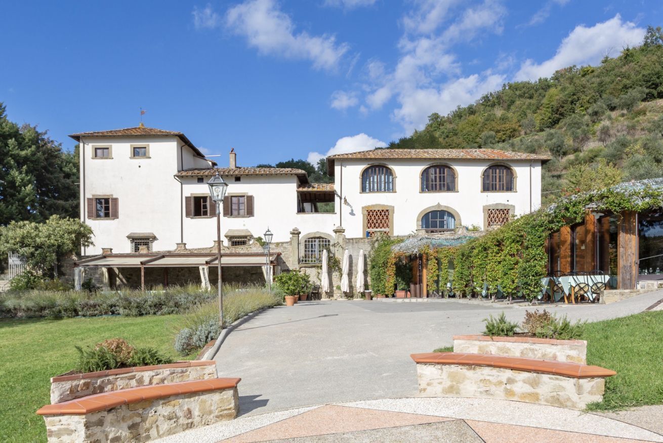 Un edificio grande e bianco con tetto in tegole, un portico coperto e un vialetto in pietra che conduce all'ingresso.