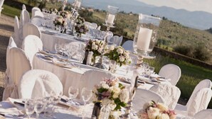 A table set for a formal outdoor event with white tablecloths, glassware, and floral centerpieces.