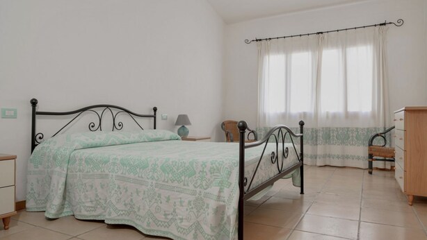 Une chambre à coucher avec un lit, une table de chevet, une commode et une fenêtre avec des rideaux.