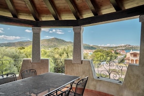 A covered outdoor area with a table and chairs, a view of a mountainous landscape, and a railing.