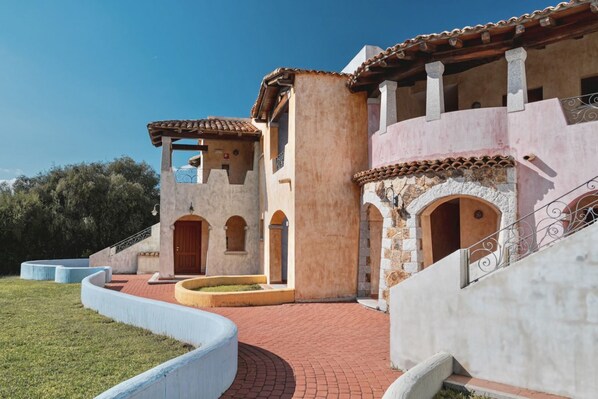 Un edificio tradicional con puertas de arco y tejado de azulejos, rodeado de un jardín ajardinado con un elemento circular de piedra.