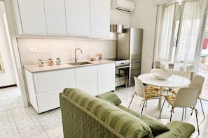 Una cocina moderna con armarios blancos, un refrigerador de acero inoxidable y un comedor con una mesa redonda y sillas.