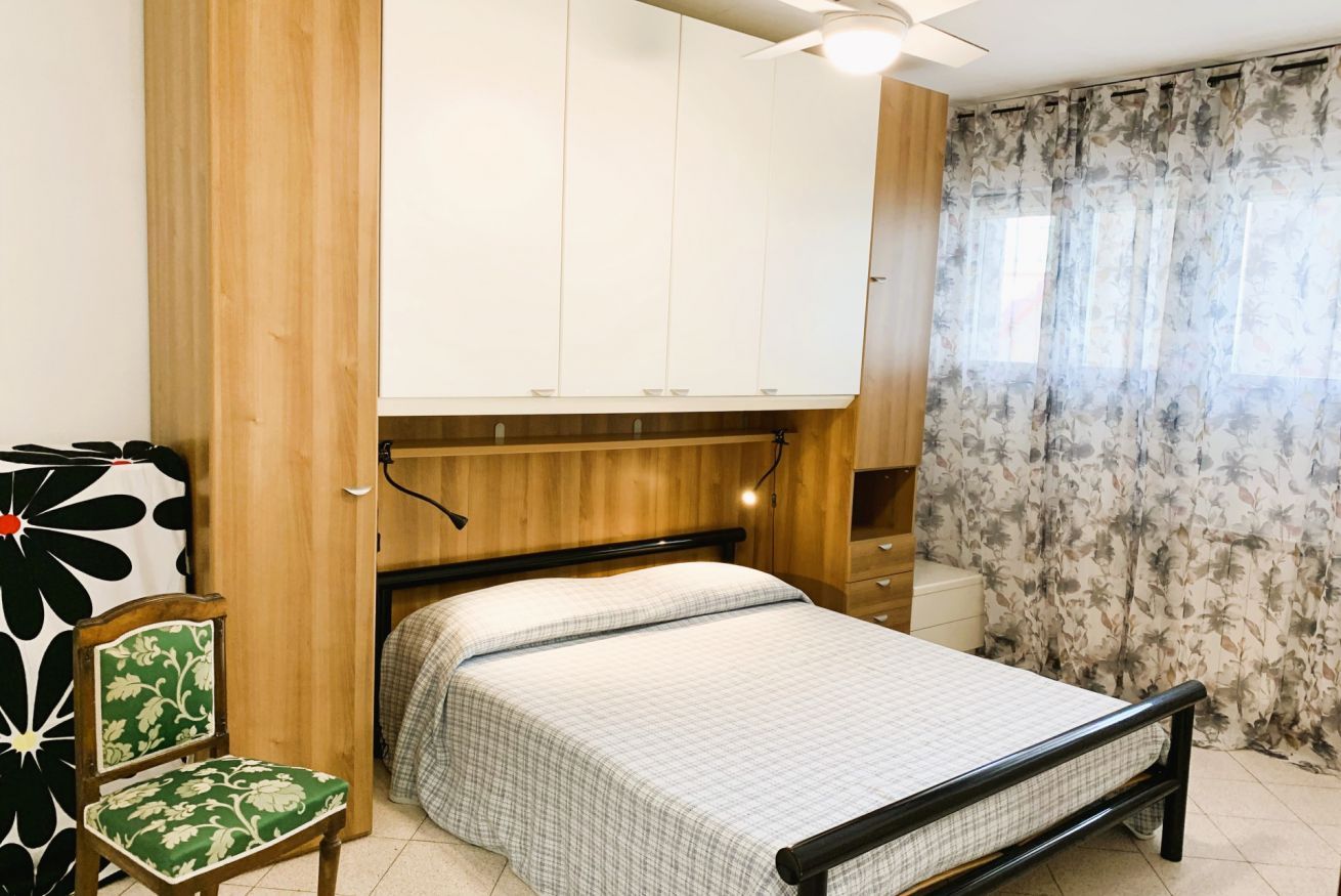 A bedroom with a bed, a wooden wardrobe, a chair, and a window with curtains.