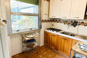 A kitchen with wooden cabinets, a gas stove, a sink, and a window with a view of greenery outside.