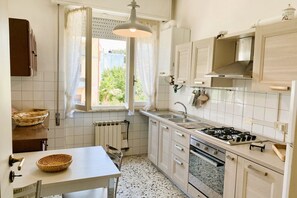 A kitchen with white cabinets, a gas stove, a sink, and a window with curtains.