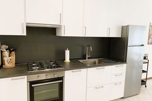 A modern kitchen with white cabinets, a stainless steel refrigerator, a gas stove, and a built-in oven.
