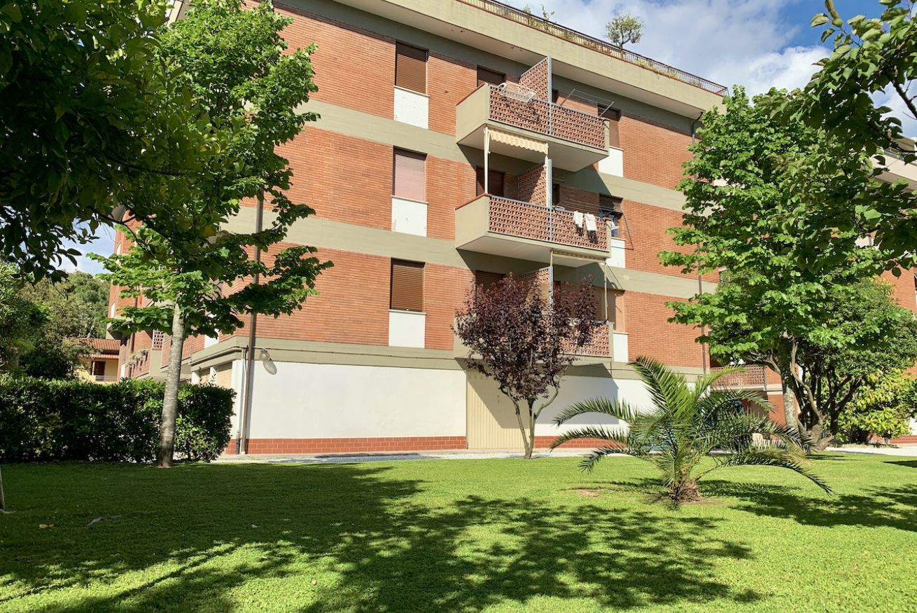 A multi-story building with a brick facade, balconies, and a well-maintained lawn.