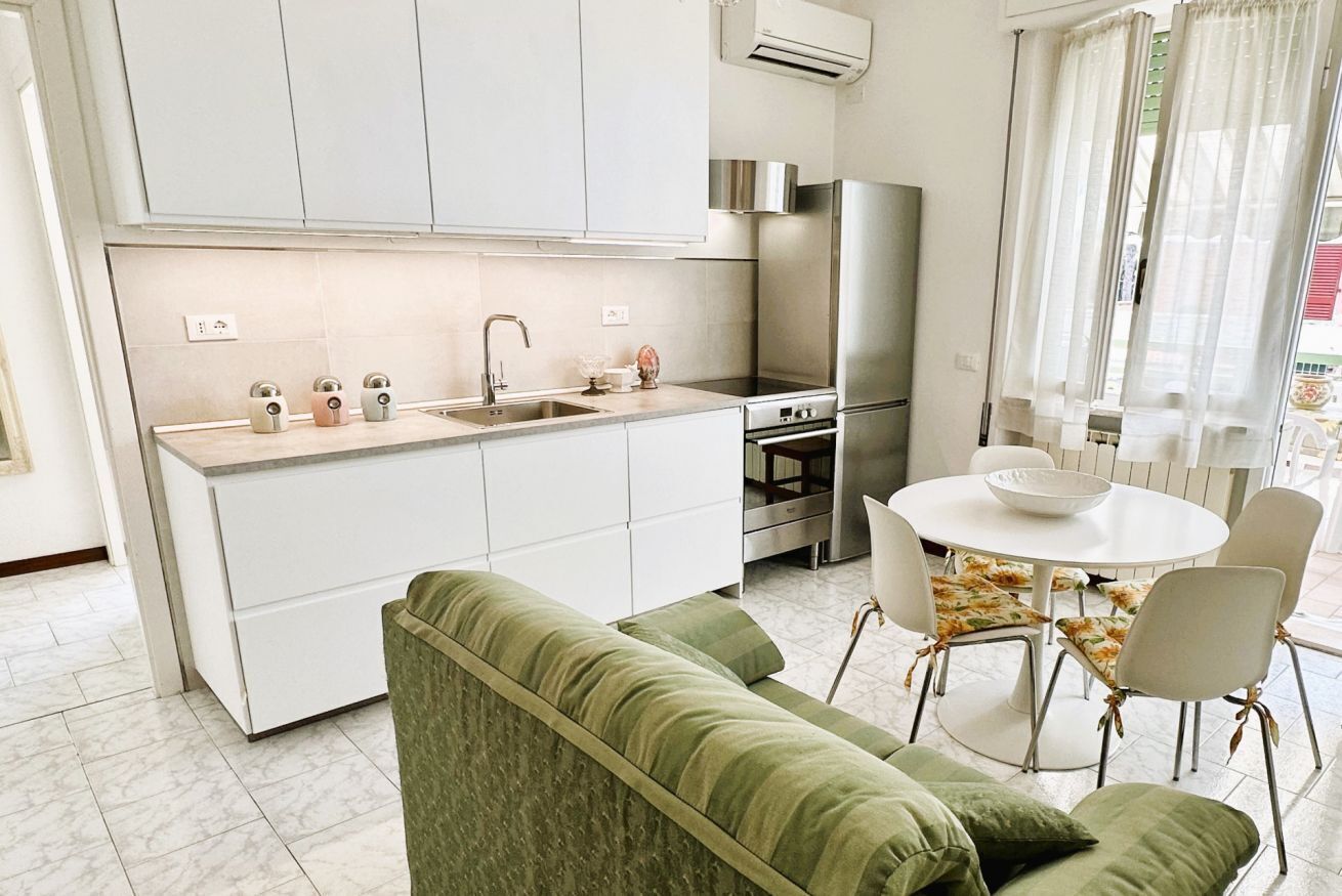 Una cucina moderna con mobili bianchi, un frigorifero in acciaio inossidabile e un'area pranzo con un tavolo rotondo e sedie.