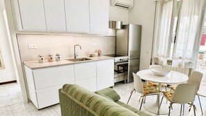A modern kitchen with white cabinets, a stainless steel refrigerator, and a dining area with a round table and chairs. - Apartment 3 rooms furnished with taste, 55/60mq, kitchenette / living room and double sofa bed or two sofa beds, matrimonial bedroom, double bedroom, bathroom.Included of:<br>tv, <br><b>washing machine<b>, <br><b>balcony or small garden <b>, <br>parking  (Massa)