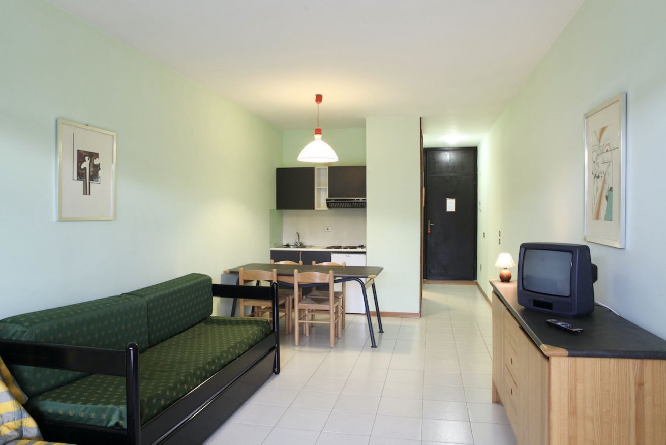 A compact living space with a bed, kitchenette, dining area, and a television.