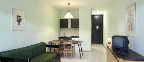 A compact living space with a bed, kitchenette, dining area, and a television.