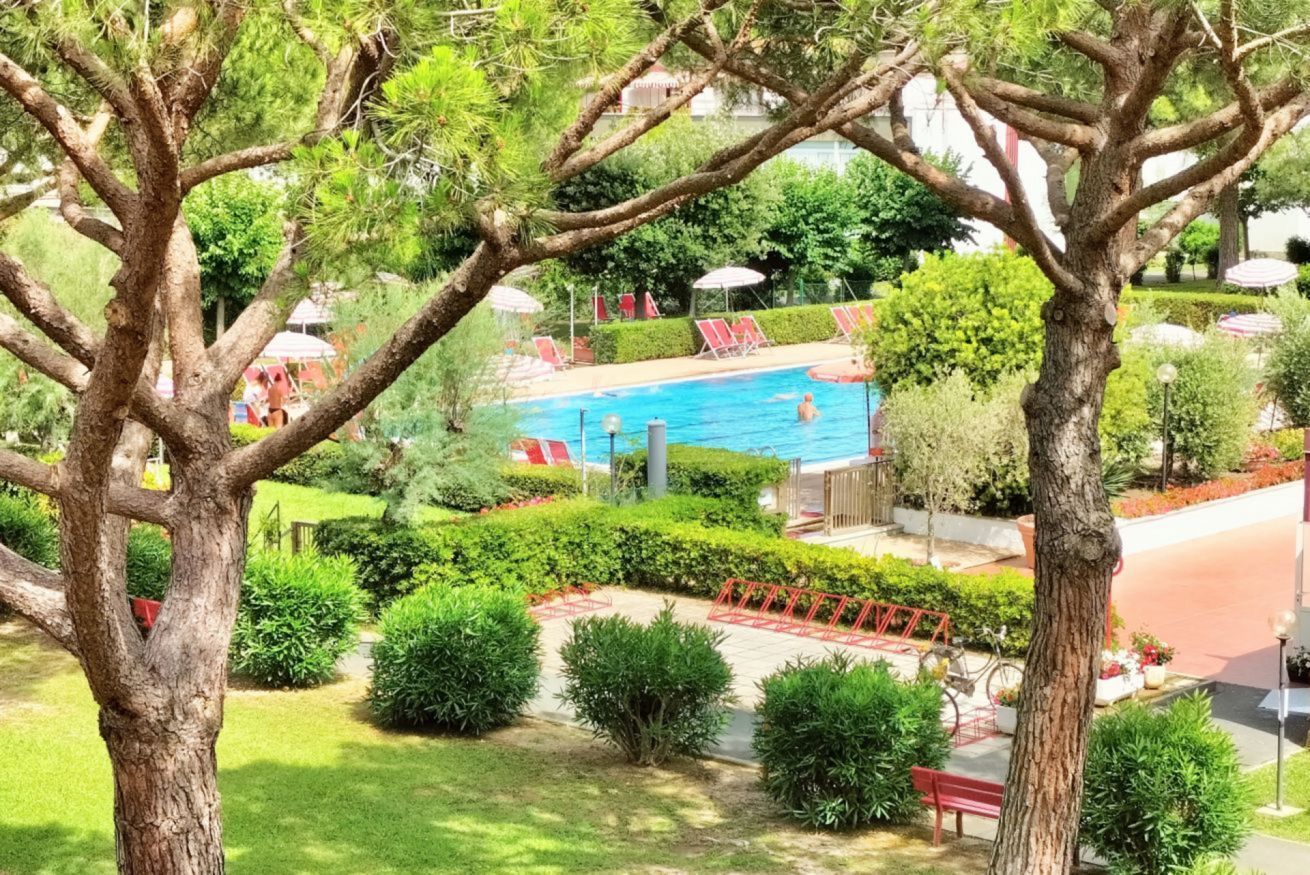 En swimmingpool omgivet af frodig vegetation, med røde liggestole og parasoller.