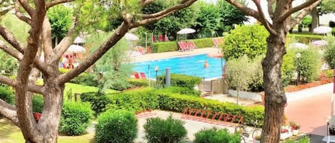 A swimming pool surrounded by lush greenery, with red lounge chairs and umbrellas.