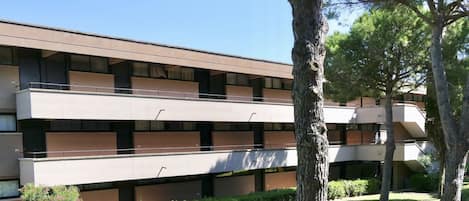 A multi-story building with a flat roof, balconies, and a well-maintained lawn with trees.