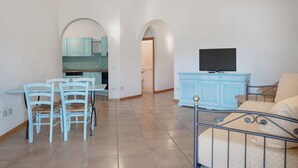 A living room with a TV, a dining area with chairs, and a kitchen with blue cabinets. - Two-room apartment for 4 people composed of large living room with kitchenette and double sofa bed, double bedroom, two bathrooms. <br>equipped with: <br>LCD TV, <br>washing machine,<br>dishwasher,<br>air conditioning,<br> table and chairs for outdoor us (Marinella)