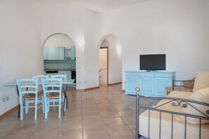 A living room with a TV, a dining area with chairs, and a kitchen with blue cabinets.