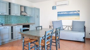 A compact kitchen with blue cabinets, a dining table with chairs, and a sofa. - Two-room apartment for 4 people composed of large living room with kitchenette and double sofa bed, double bedroom, two bathrooms. <br>equipped with: <br>LCD TV, <br>washing machine,<br>dishwasher,<br>air conditioning,<br> table and chairs for outdoor us (Marinella)