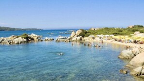 Una spiaggia rocciosa con acque cristalline, persone che nuotano e ombrelloni.