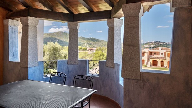 A covered outdoor seating area with a table and chairs, large windows, and a view of a distant building. - Two-room apartment for 4 people composed of large living room with kitchenette and double sofa bed, double bedroom, two bathrooms. <br>equipped with: <br>LCD TV, <br>washing machine,<br>dishwasher,<br>air conditioning,<br> table and chairs for outdoor us (Marinella)