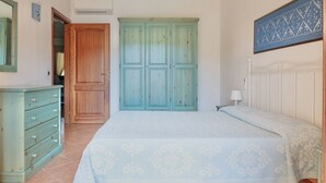 A bedroom with a bed, a dresser, a wardrobe, and a wall-mounted lamp. - Two-room apartment for 4 people composed of large living room with kitchenette and double sofa bed, double bedroom, two bathrooms. <br>equipped with: <br>LCD TV, <br>washing machine,<br>dishwasher,<br>air conditioning,<br> table and chairs for outdoor us (Marinella)