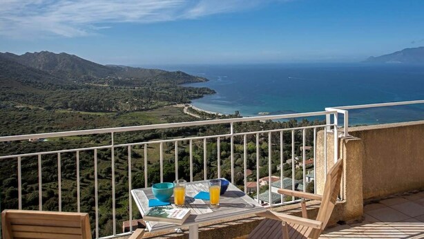 Ein Balkon mit Tisch, zwei Stühlen und Blick auf das Meer und die Berge.