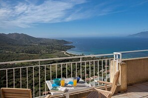 A balcony with a table, two chairs, and a view of the sea and mountains. - Villa Cléa (Saint-Florent)